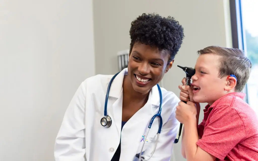 Boy with hearing aid checks his physician’s ear.