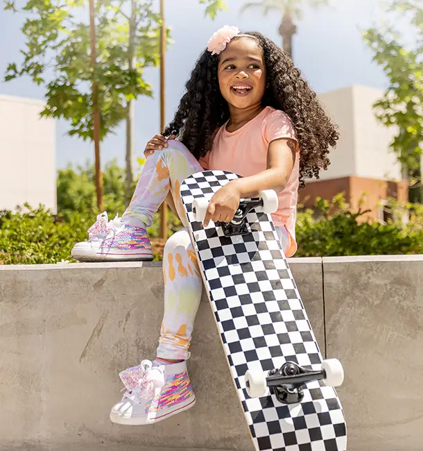 A young girl sitting on a wall holding a skateboard